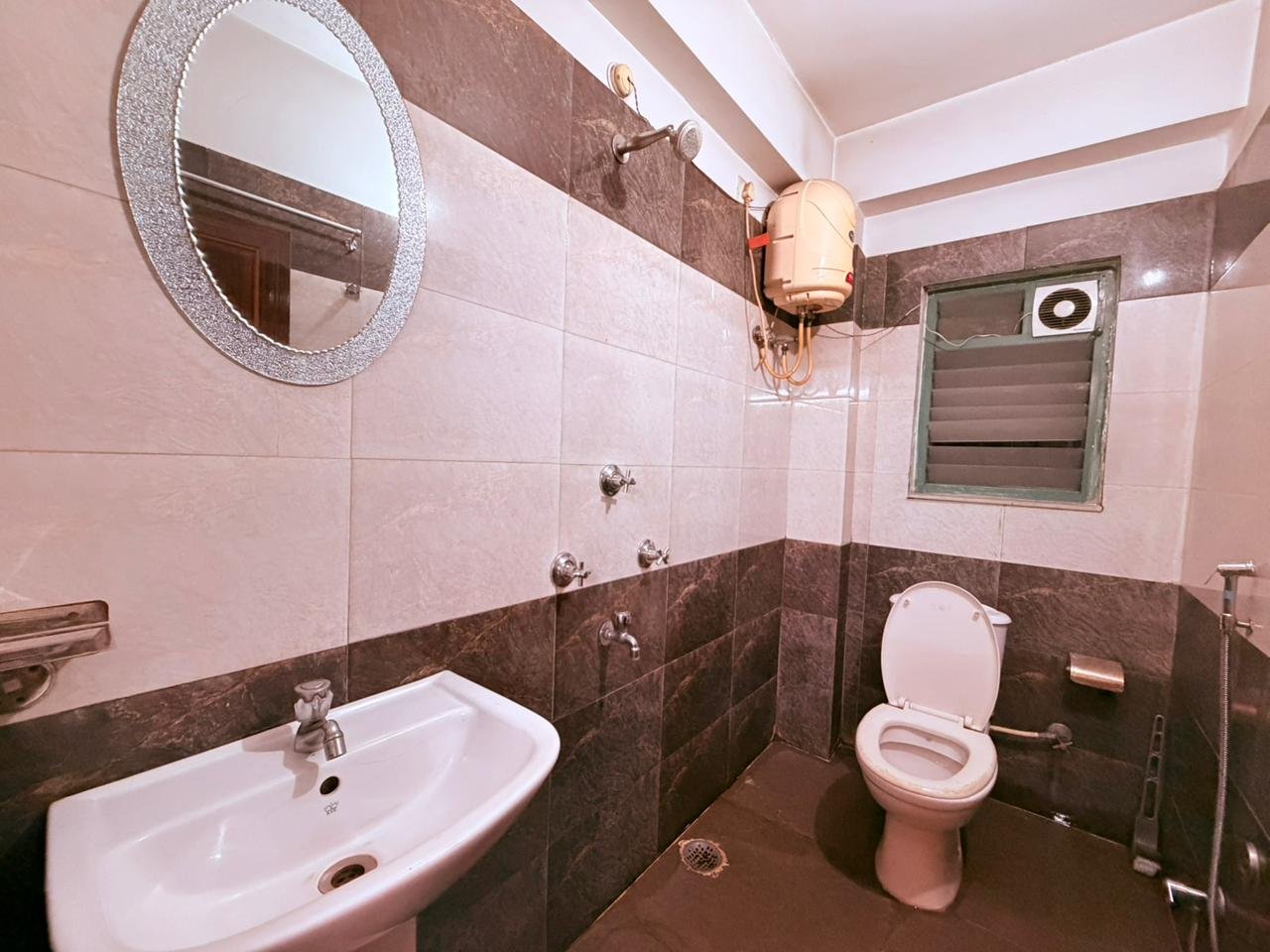 Guest bathroom with wash basin, round mirror, geyser and western toilet