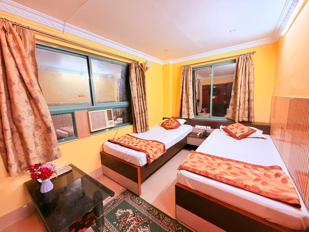 Twin-bed AC room with curtained windows and a side table with flowers